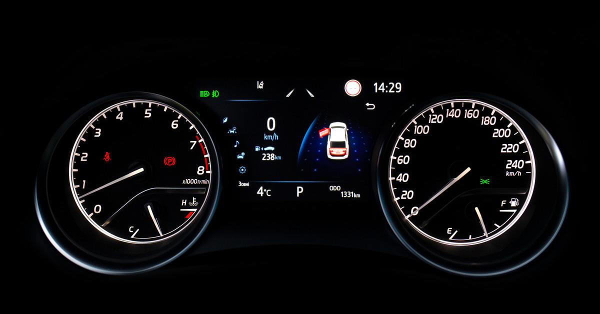 A close up view of a Toyota's dashboard. It's dark and the icons, silver letters, and numbers light up the dash.