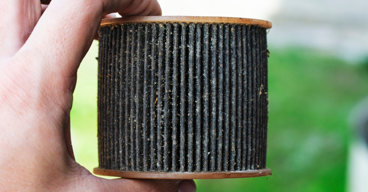 A person holds up a clogged oil filter up to the camera. The filter is dark and dirty, worn down over time.