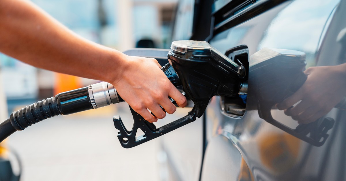 A person's hand grips a gas pump as its going inside of a car's gas tank. The car is silver and the pump is black.