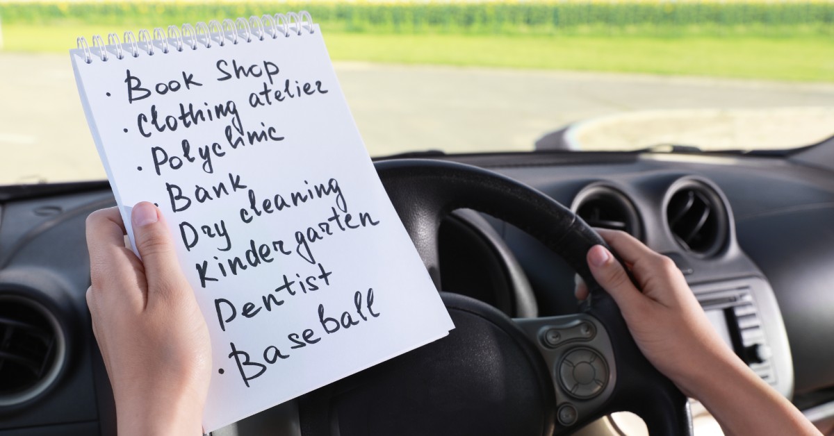 A person with one hand on their pickup truck's steering wheel and one hand on a list of errands to run.