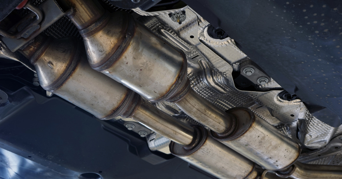 A catalytic converter is installed on the undercarriage of a modern car. Some parts are spotless while others are dirty.