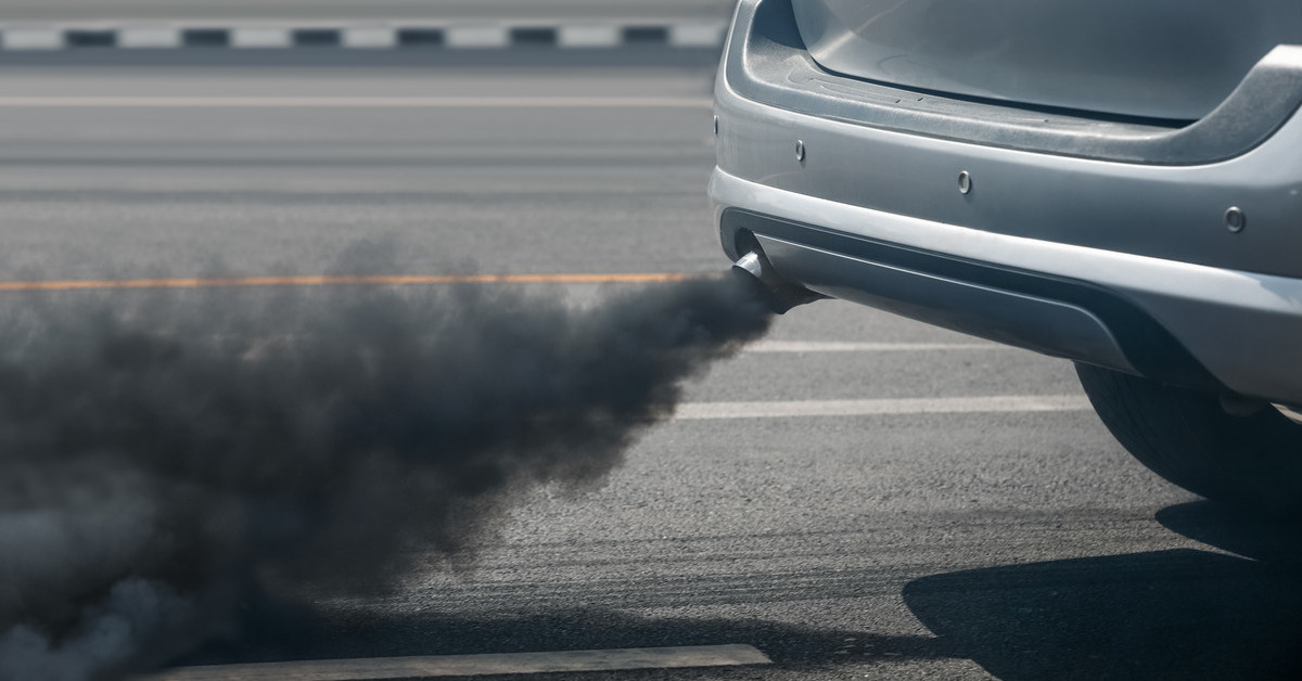 A car driving on the road has an exhaust pipe and there are powerful, dark clouds of exhaust coming out.