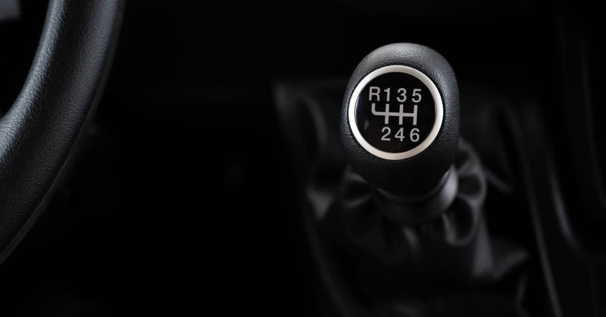 A black gear shift in a car is front and center while there's an edge of the steering wheel in the corner.