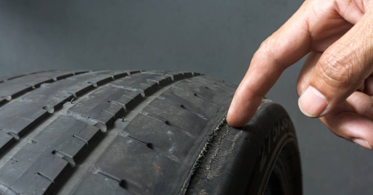 A person has their finger on the edge of a worn down tire where the tire tread is almost completely gone.