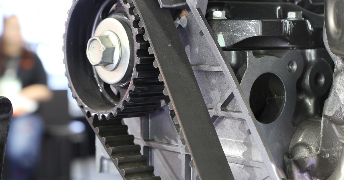 A close up view of a diesel engine timing belt with other components next to it, and a blurry person in the background.