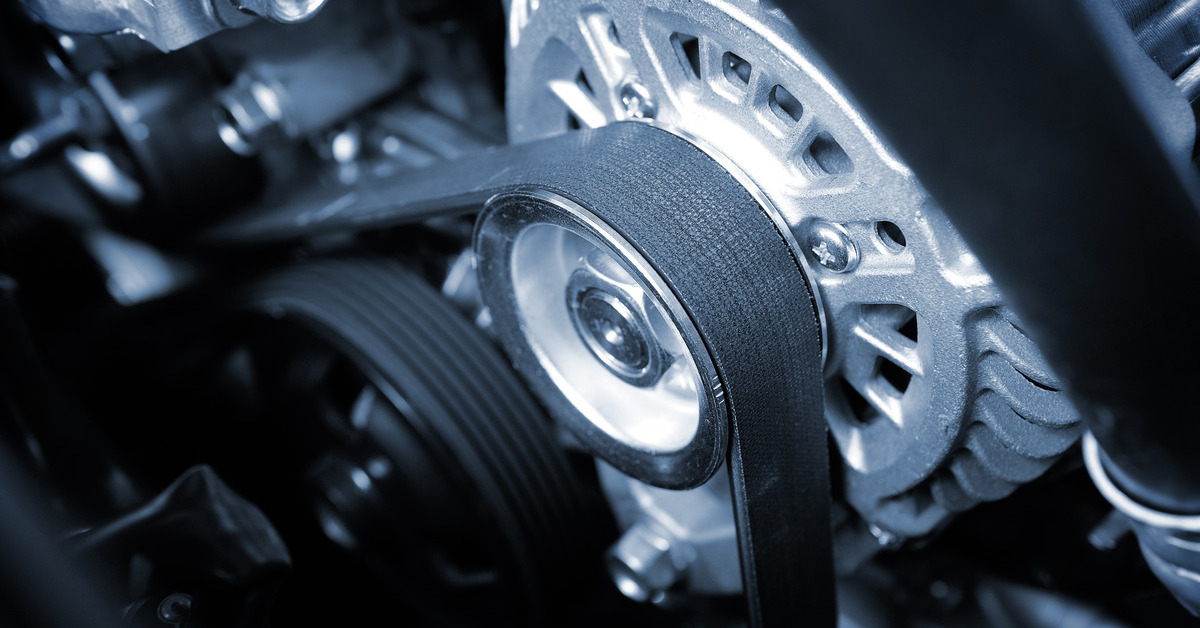 A smaller, thinner timing belt is in place under the hood of a car. The belt is black and the other components are silver.