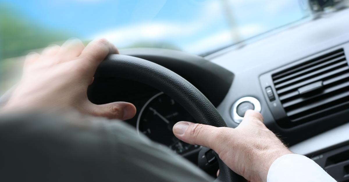 A person behind a steering wheel is turning it quickly. Through the front window there are blurred clouds and sky.