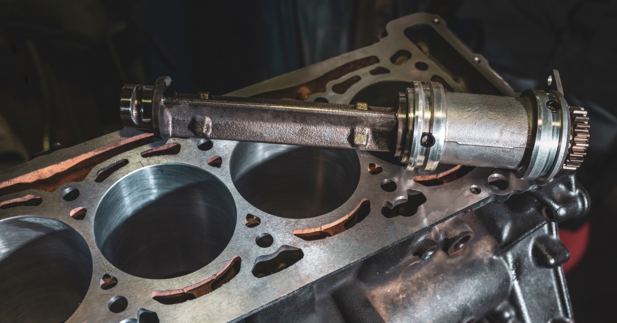 A person holding a disassembled metal engine block with exposed cylinder chambers and internal mounting points.